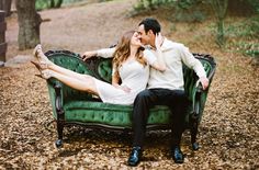 a man and woman sitting on top of a green couch in the middle of a forest