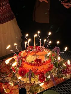 a birthday cake with lit candles on it sitting on a table in front of people