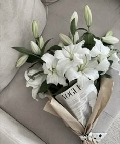 a bouquet of white flowers sitting on top of a couch next to a newspaper bag