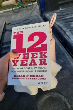 a person holding up a book about the 12 year plan on top of a car