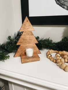 a small wooden christmas tree sitting on top of a mantle next to a candle holder