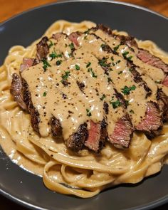 a plate of pasta with steak and sauce on it, sitting on a table top