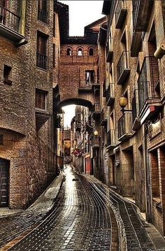 an alley way with brick buildings and cobblestone roads in the middle, surrounded by stone walls