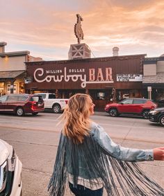 a woman walking down the street in front of a bar with cars parked on it