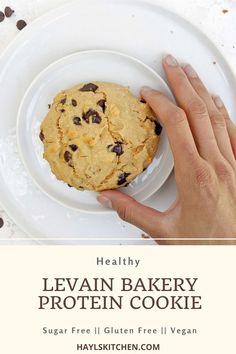 a person holding a cookie on top of a white plate with chocolate chips around it