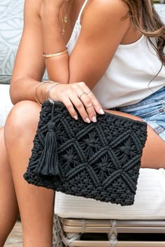 a woman sitting on top of a white couch holding a black crochet purse