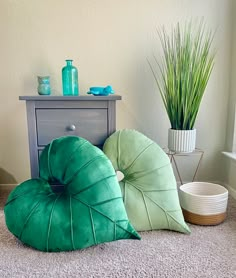 three green pillows sitting on top of a carpet next to a dresser and potted plant