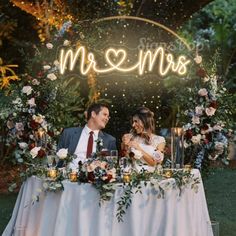 a man and woman sitting at a table under a neon sign that says mr and mrs