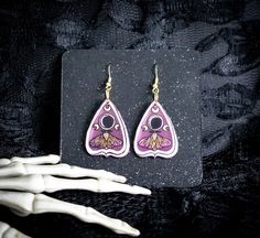 a pair of pink and yellow earrings sitting on top of a black table next to a white hand