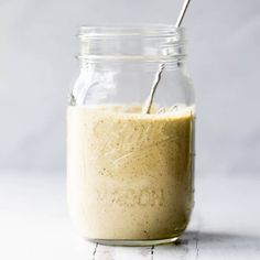 a glass jar filled with dressing sitting on top of a white counter next to a metal spoon