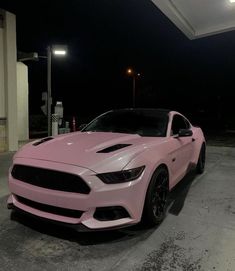 a pink ford mustang parked in front of a gas station at night with the lights on