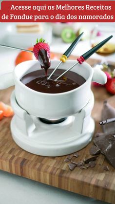 chocolate fondant being dipped with tongs in a bowl on a cutting board next to fruit