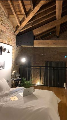 a bed with a laptop on top of it in a room next to a brick wall