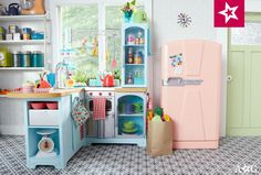 a toy kitchen with pink refrigerator and blue cabinets