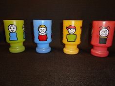 four different colored cups with cartoon faces on them sitting next to each other in front of a black background