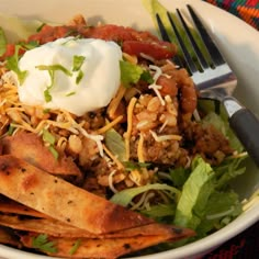 a white bowl filled with lots of food next to a fork and knife on top of a table