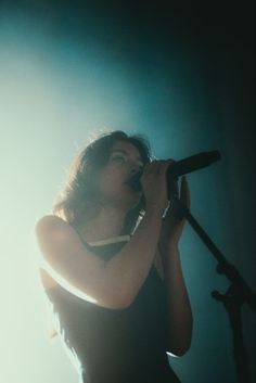 a woman singing into a microphone while standing in front of a light on a stage