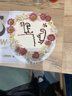 a cake decorated with flowers on top of a wooden table next to a glass of wine