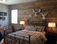 a woman taking a photo of a bed in a room with wood walls and deer head mounted on the wall