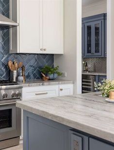 a kitchen with marble counter tops and stainless steel oven hoods, white cabinets and blue backsplash