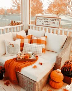 the porch is decorated for fall with pumpkins and leaves on the floor, along with white wicker furniture