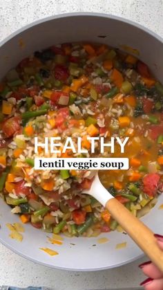 a white bowl filled with vegetables and rice next to a wooden spoon on top of a table