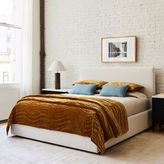 a bedroom with white brick walls and a bed in the middle is decorated with blue and gold throw pillows