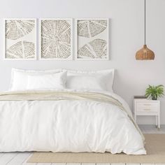 a bed with white sheets and pillows next to two pictures on the wall above it