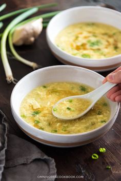 two white bowls filled with soup on top of a wooden table next to green onions