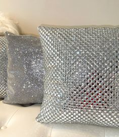 three silver pillows sitting on top of a white couch next to a pillow with sequins