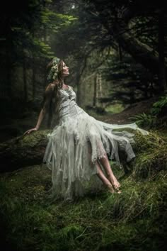 a woman in a white dress sitting on top of a moss covered tree trunk with her eyes closed