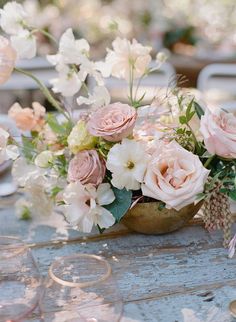 an arrangement of flowers in a bowl on a table with wine glasses and napkins