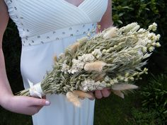 a woman in a white dress holding a bunch of dried flowers