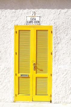 a yellow door is in front of a white building with shutters and a sign above it