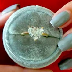 a woman's hand holding a ring with a heart shaped diamond on it