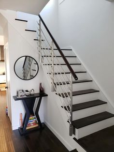 there is a mirror on the wall next to the stair case in this room with white walls and wood floors