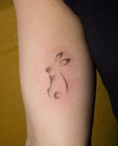 a small rabbit tattoo on the right arm and leg, with an outline of a bunny behind it