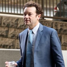 a man in a suit and tie is holding a drink while walking down the street