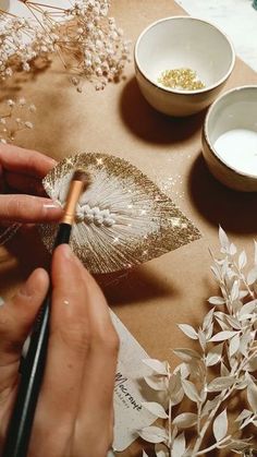 a person is painting leaves on a piece of paper with gold paint and some white flowers