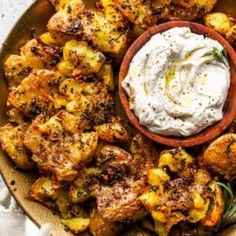 a plate filled with potatoes and some dip on top of the other side, next to a small bowl of ranch dressing