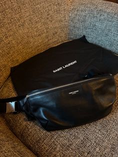 This sleek and stylish Saint Laurent leather belt bag is the perfect accessory for any fashion-forward individual. Made from high-quality leather, this bag is both durable and chic. It features a black exterior with silver hardware, as well as a black lining and handle/strap. With its unisex design, this bag is suitable for both men and women, and its versatile style makes it the perfect addition to any outfit. Whether you're hitting the town or running errands, this belt bag will keep your essentials close at hand. This bag is in excellent condition. My husband only wore it a handful of times and just decided it wasn’t for him. Black Leather Evening Belt Bag, Black Leather Belt Bag For Evening, Leather Belt Bag With Branded Hardware, Designer Leather Belt Bag For Travel, Designer Leather Belt Bag For Evening, Classic Black Soft Leather Belt Bag, Luxury Black Leather Belt Bag, Leather Crossbody Belt Bag With Branded Hardware, Classic Black Belt Bag For Business