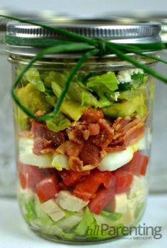 a glass jar filled with lots of salads and meat on top of lettuce