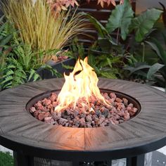 a fire pit sitting on top of a wooden table next to flowers and plants in the background