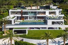 an aerial view of a large white house surrounded by palm trees and greenery in the foreground