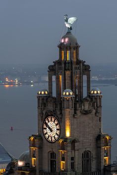 a large clock tower lit up at night with lights on it's sides and the ocean in the background