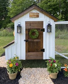 a small white shed with two potted plants and a wreath on the front door