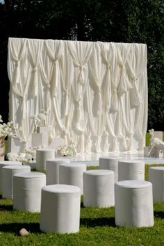 a bunch of white vases sitting in front of a wall with drapes on it