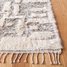 a white and gray rug with fringes on top of a wooden floor next to a hard wood floor