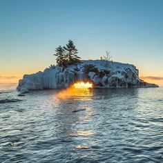 the sun is setting on an ice covered island in the middle of the ocean with trees growing out of it