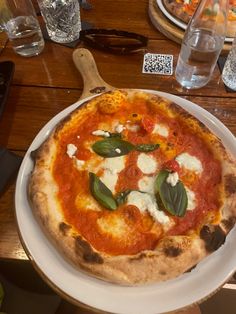 a pizza sitting on top of a white plate covered in cheese and sauce with basil